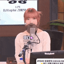 a girl with red hair is sitting in front of a microphone and a monitor with the number 1045 on it