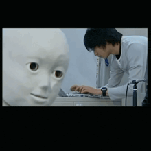 a man is typing on a laptop next to a white mannequin head
