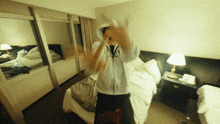 a man in a hoodie is standing in a hotel room with his hands in the air
