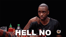 a man is sitting at a table with bottles of hot sauce and says hell no