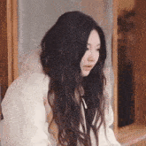a woman with long dark hair is wearing a white jacket and looking down .