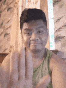 a man in a green tank top is making a funny face with his hands .