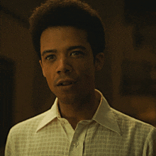 a man in a white shirt looks at the camera with a serious look on his face