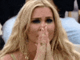 a woman with blonde hair is covering her mouth with her hands .