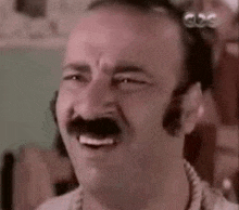 a man with a mustache is smiling and making a face .