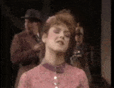 a woman in a pink dress is singing with a man in a hat behind her