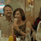 a woman is eating an ice cream cone while a man looks on
