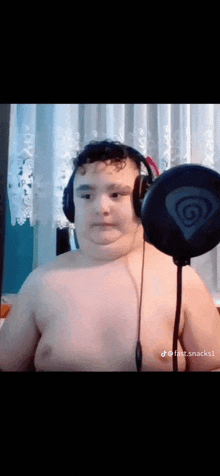 a shirtless boy wearing headphones and a microphone is standing in front of a microphone .