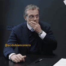 a man in a suit and tie covering his mouth with his hand with the hashtag acidobianconero