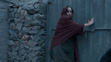 a woman in a red shawl stands in front of a wooden door