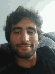 a man with a beard is sitting on a couch smiling