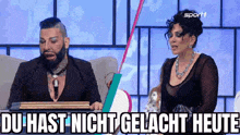 a man and a woman are sitting next to each other with the words du hast nicht gelacht heute written on the screen .