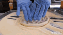 a person wearing blue gloves is making a pizza dough