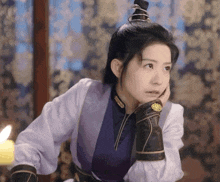 a woman in a purple and white costume is sitting in a room with her hand on her face .