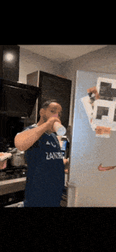 a man in a zanzibar shirt is drinking from a cup in a kitchen