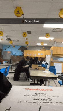 a man sits at a table in a classroom with the words " it 's crab time " above him