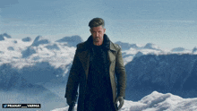 a man in a trench coat stands on top of a snow covered mountain with the name pranay varma below him
