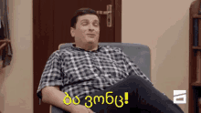 a man in a plaid shirt is sitting in a chair with his legs crossed and says do 3mbg !