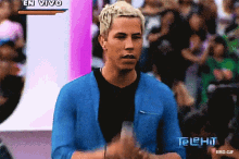 a man in a blue jacket stands in front of a crowd with a telehit logo on the bottom