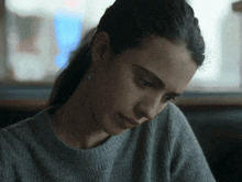 a woman wearing a grey sweater and earrings is looking down