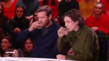two men are sitting at a table drinking water from glasses .