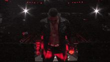 a man in a leather jacket is standing in a dark room with a light shining on him