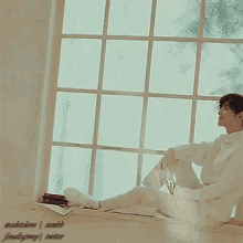 a man in a white shirt sits on a window sill with his legs crossed