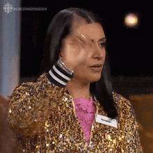 a woman wearing a gold sequined jacket and a pink shirt is covering her face with her hand .