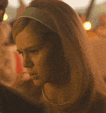 a woman wearing a headband and a pearl necklace looks angry
