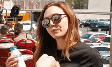 a woman wearing sunglasses is holding a bottle of water and looking at the camera .