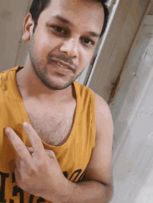 a man wearing a yellow tank top that says ' the ' on it is giving a peace sign