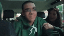 a man in a green sweatshirt is riding on the back of a woman 's shoulders in a car .