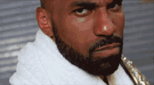 a man with a beard and a white towel around his neck looks at the camera