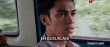 a man sitting in a car with the words eh busukah behind him