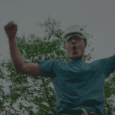 a man wearing a blue shirt and a white helmet holds his arms up in the air