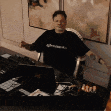 a man wearing a black shirt that says experiments is sitting at a desk
