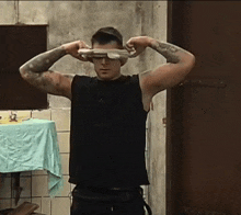 a man in a black tank top is covering his eyes with a glove