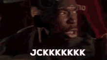 a man is driving a car with the words jckkkkkk written on the screen behind him .