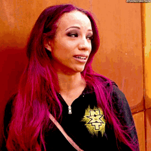 a woman with pink hair is wearing a black shirt with a yellow x on it