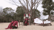 a man in a red robe sits on a throne next to a clock