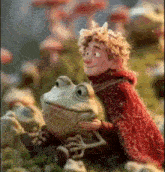 a boy in a red cape is sitting on a frog 's lap .
