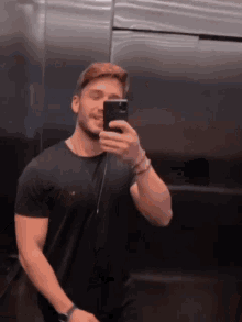 a man in a black shirt is taking a picture of himself in the mirror