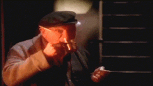 a man wearing a hat is smoking a cigarette in a dark room