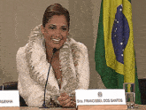 a woman in a fur coat sits at a table with a name tag that says francisbel dos santos