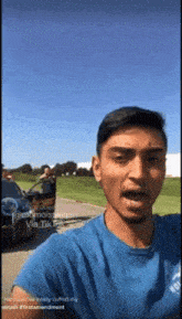 a man in a blue shirt is standing in front of a car with a sign that says " she 's a cutie "