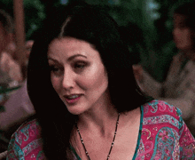 a woman with long dark hair is wearing a pink and blue top and a necklace .