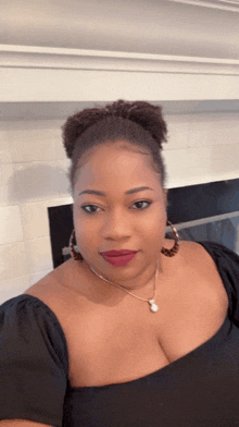 a woman wearing a black off the shoulder top and earrings looks at the camera