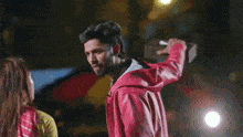 a man in a red jacket is holding a pizza box over a woman in a car .