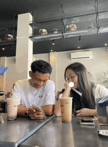 a man and a woman are sitting at a table with drinks and looking at their phones