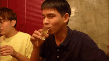 a man is drinking from a shot glass while another man watches .